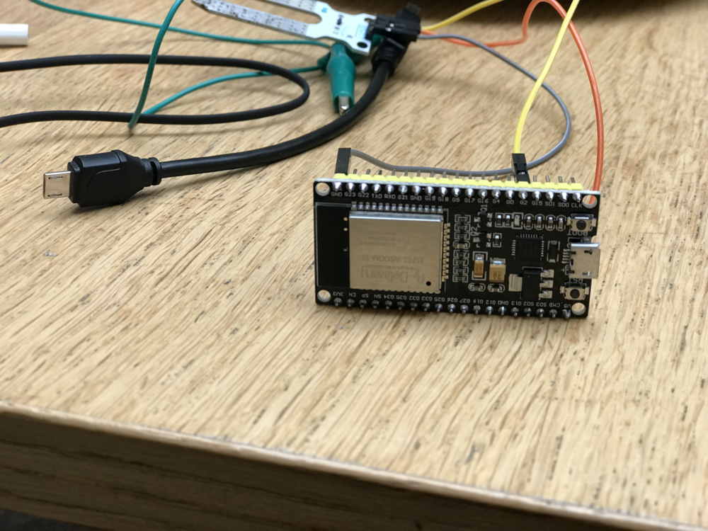 an esp32 micro-controller with dupont cables one yellow linked to pin g2 and one grey gnd, in the background there is a moisture sensor